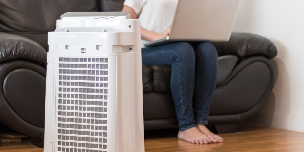 Air purifier in living room with person using laptop, highlighting indoor air quality solutions for homes in Bloomfield Hills.