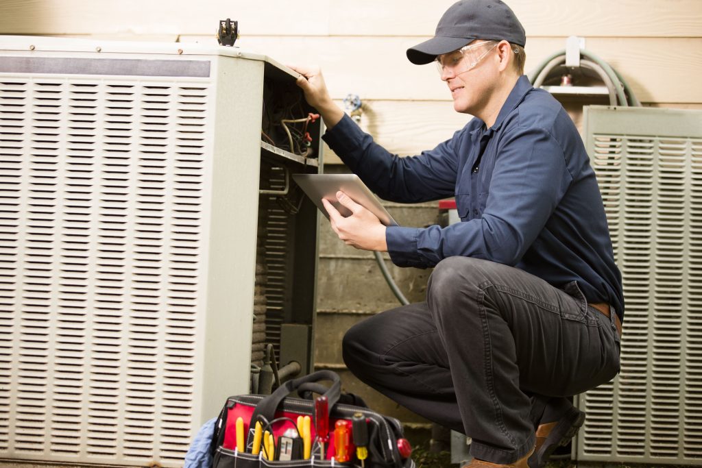 HVAC technician inspecting outdoor cooling unit with tablet and tool bag, emphasizing expert HVAC services in Basil Park.