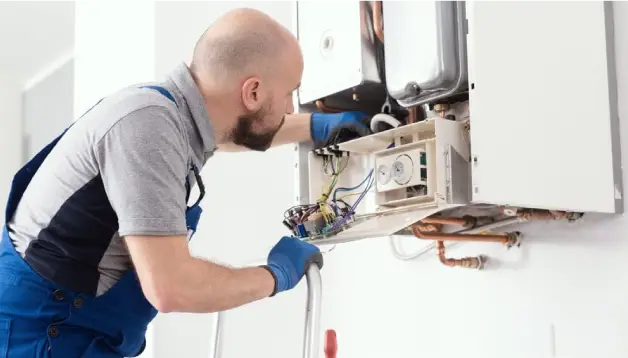 Technician performing heater repair on a wall-mounted unit, wearing gloves and inspecting internal components for maintenance and efficiency.