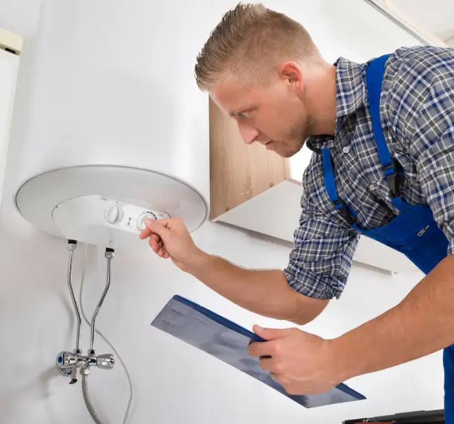 Technician adjusting settings on a water heater while reviewing documentation for compliance and installation standards.