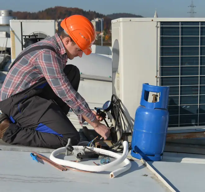 HVAC technician in orange hard hat servicing an outdoor air conditioning unit with tools and equipment on a rooftop in Lake Orion.