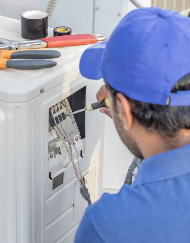Technician performing air conditioning maintenance on a residential unit, using a screwdriver to ensure efficient and safe operation.