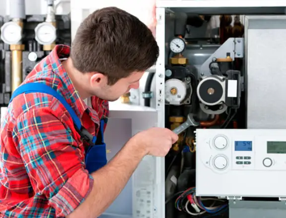 Technician repairing a heating system, focused on internal components, demonstrating HVAC maintenance services for Comfort Plus in Lake Orion.