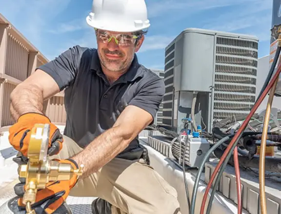 HVAC technician performing maintenance on air conditioning unit, wearing safety gear and gloves, emphasizing Comfort Plus's commitment to efficient heating and cooling solutions.