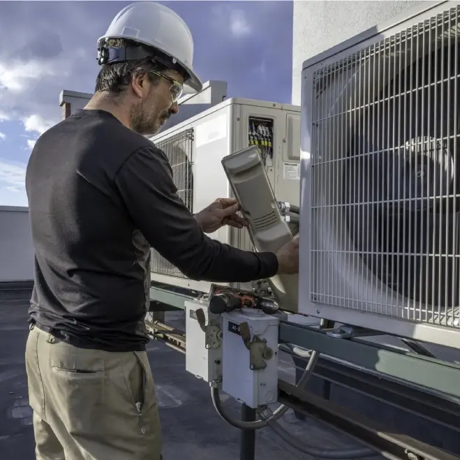 Technician performing maintenance on HVAC unit, wearing safety helmet and working on outdoor cooling system, emphasizing Comfort Plus's commitment to expert HVAC services in Lake Orion.