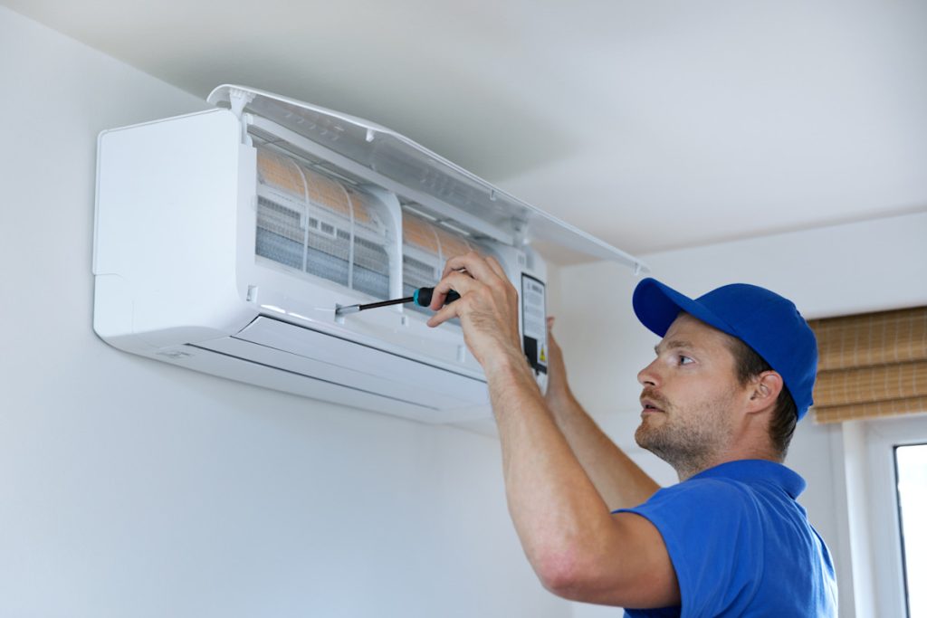 Technician performing maintenance on a wall-mounted air conditioning unit, emphasizing HVAC service expertise and system optimization for home comfort.