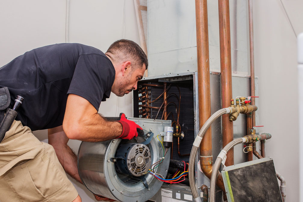 HVAC technician repairing a furnace motor, surrounded by copper pipes and electrical components, emphasizing emergency heating repair services in Basil Park.